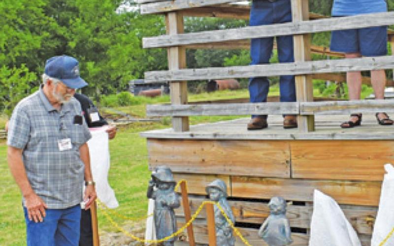 DEANVILLE HERITAGE FOUNDATION members, Tom and Patsy Simek, name each of the 14 Orphan Train riders who resided in Burleson County and uncover a statue representing each of the riders. Also pictured on the platform is foundation president, Tommy Ryan. -- Tribune photo by Roy Sanders