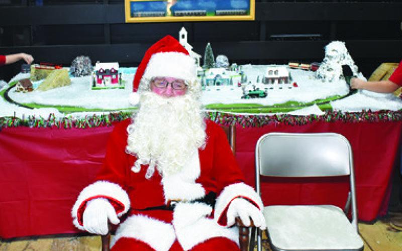 SANTA CLAUS GREETS visitors as children play behind him on Saturday at the Deanville Heritage Foundation’s Hot Cocoa, Cookies &amp;amp; Santa celebration at the Deanville Depot.