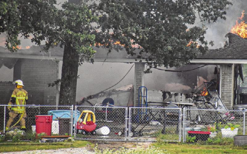 FLAMES ARE VISIBLE on Thursday, July 16, from this house fire off F.M. 1362 South near Cooks Point. Tribune photo by Roy Sanders