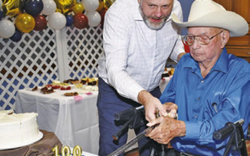 LONNIE FRANK cuts the cake with a sword in celebration of his 100th birthday.