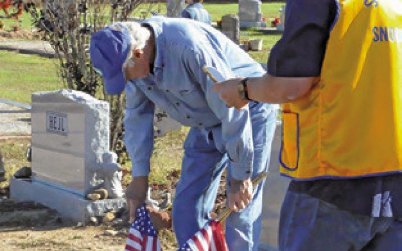 SNOOK LI ONS CLUB members Steve Tunnell and John Pollock place flags at a veteran’s grave in the Snook Cemetery on Saturday. Tribune photo by Denise Squier
