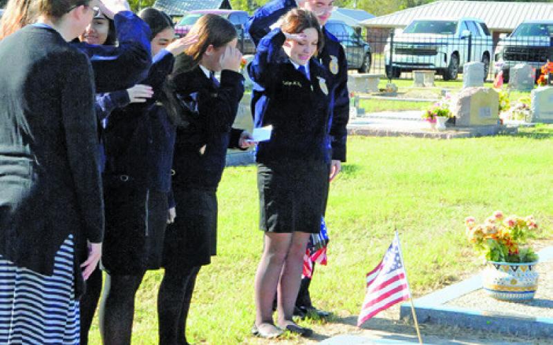 SNOOK HIGH SCHOOL FFA MEMBERS salute this veteran’s grave after they placed a flag on it last Saturday morning. Tribune photo by Denise Squier