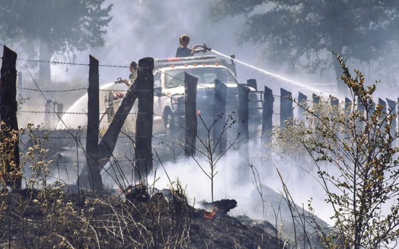 FIRFIGHTERS SPRAY WATER ALONG the fence line last Friday off County Road 324. More than 30 acres burned. Tribune photo by Roy Sanders