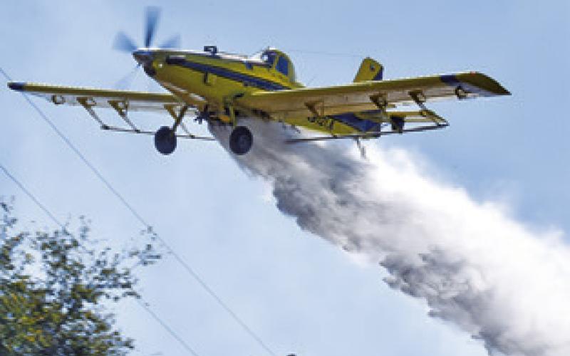 KEN LAUDERDALE drops water on this blaze on Friday off County Road 324. Tribune photo by Roy Sanders