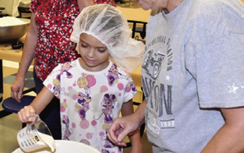 LAURA SEBESTA helps Kinsley Crump mix the dough for the kolaches at this kolache baking lesson on Saturday at Snook Elementary School. Sharon Kovar, left, observes.