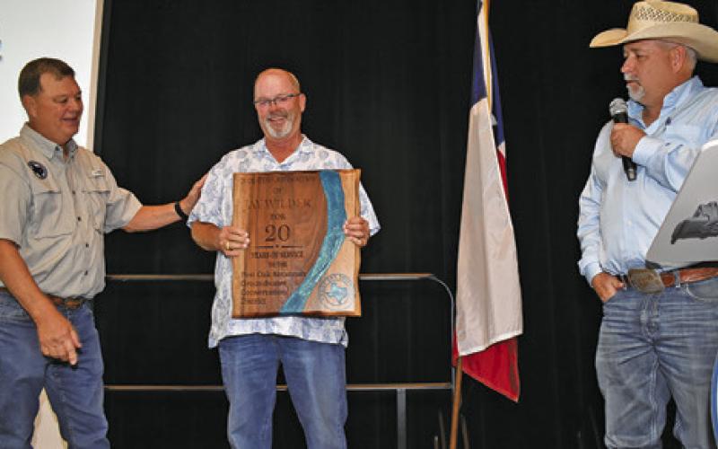 POSGCD BOARD PRESIDENT Jay Wilder is presented this plaque for his 20 years of service on the board by POSGCD General Manager Gary Westbrook, left, and Burleson County Judge Keith Schroeder.