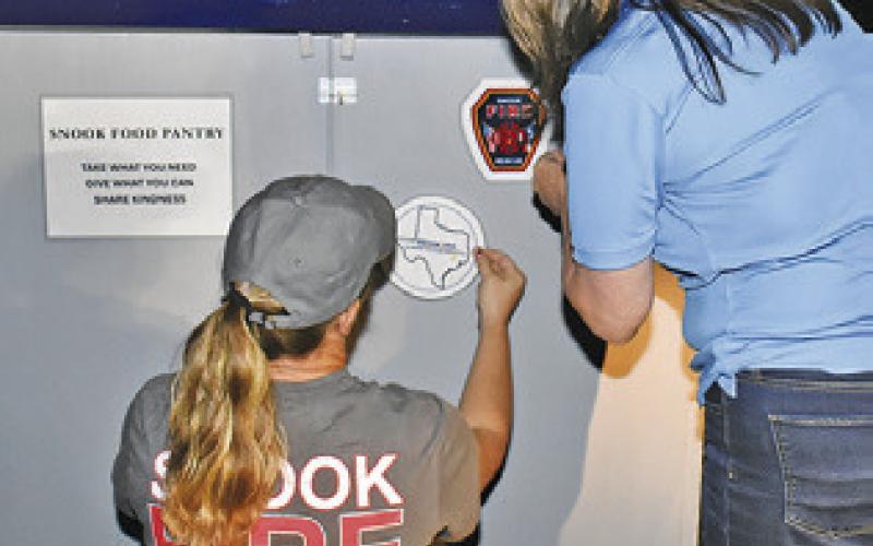 BETH COLLINS of Snook Volunteer Fire Department and Cindy Jarrott of Snook EEA place these labels on the food pantry.