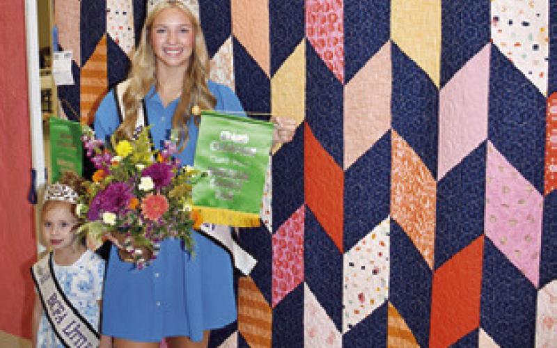 BURLESON COUNTY FAIR Queen Hadleigh Novosad displays her grand champion quilt from the Burleson County Fair and is joined by Little Miss Avery Grace Freeman.