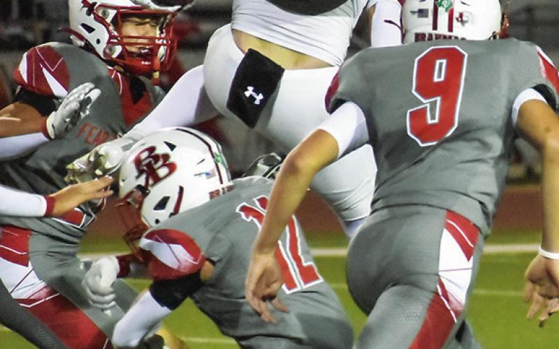 COY BECKA OF Caldwell leaps over these Bellville defenders for yardage. Tribune photo by Roy Sanders
