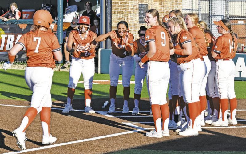 CALDWELL’S EMILY SMITH IS GREETED by the rest of the Lady Hornets at home plate after her home run during the Lady Hornets’ 14-0 win over Smithville on Friday. -- Tribune photo by Roy Sanders