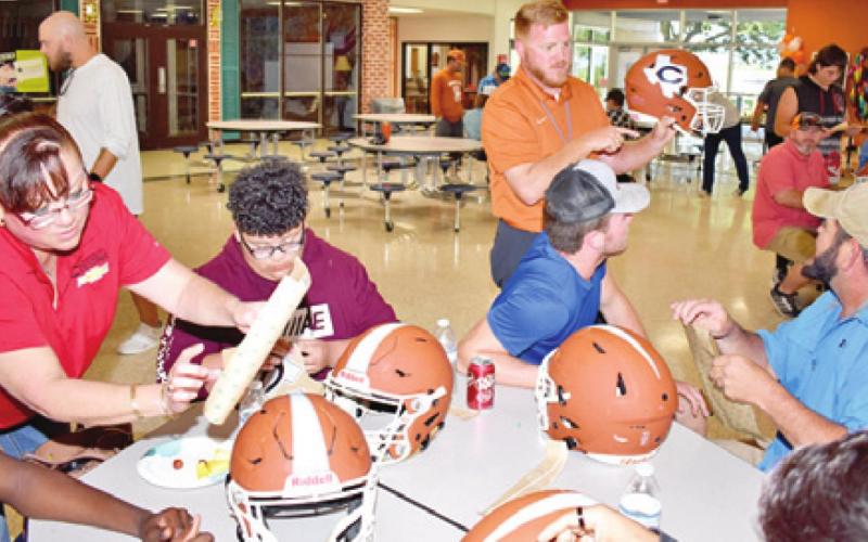 CALDWELL HEAD COACH Boone Patterson offers this demonstration on getting the decals on the Hornets’ helmets during “Helmets Withe Heroes” on Friday at Caldwell High School. Many Hornet football players involved family members in the fun.