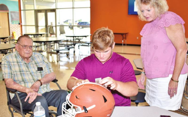 CHS’S GARRETT TITTLE places these decals on his helmet during Helmets With Heroes last Friday. Joining him were his grandfather Milton Mynar and his mother Debbie Tittle.
