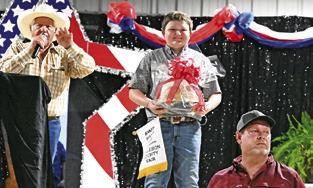 JACE HRUSKA IS PICTURED ON stage with his German Chocolate Cake and auctioneer Charles Doonan at the 2026 Burleson County Fair Association’s Baked Foods Sale. Tribune photo by Denise Squier