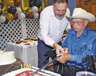 LONNIE FRANK cuts the cake with a sword in celebration of his 100th birthday.