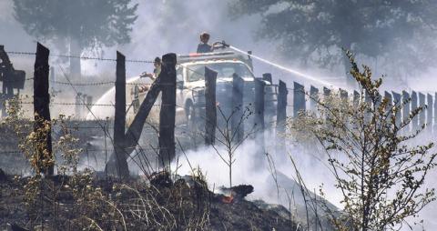 FIRFIGHTERS SPRAY WATER ALONG the fence line last Friday off County Road 324. More than 30 acres burned. Tribune photo by Roy Sanders