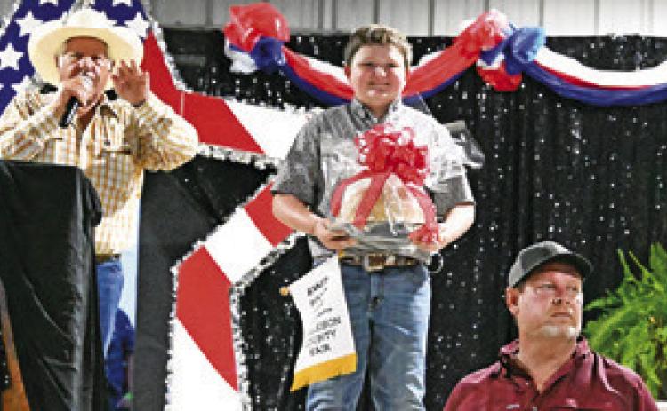 JACE HRUSKA IS PICTURED ON stage with his German Chocolate Cake and auctioneer Charles Doonan at the 2026 Burleson County Fair Association’s Baked Foods Sale. Tribune photo by Denise Squier